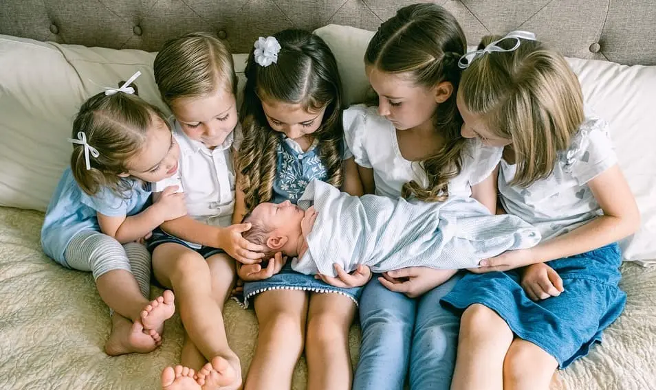 Bebe recién nacido sostenido por sus hermanos.